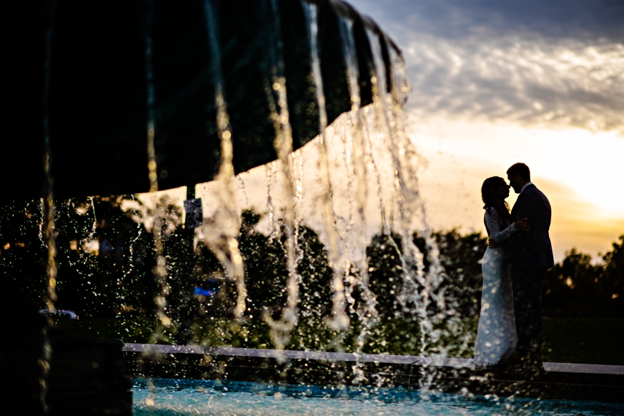 A Bride and Groom kiss by a fountain outside of the Art Museum of Philadelphia at sunset.